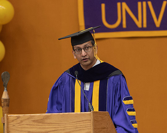 man with robe, glasses, talking at a podium