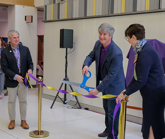 three people, two men and a women, one cutting a ribbon