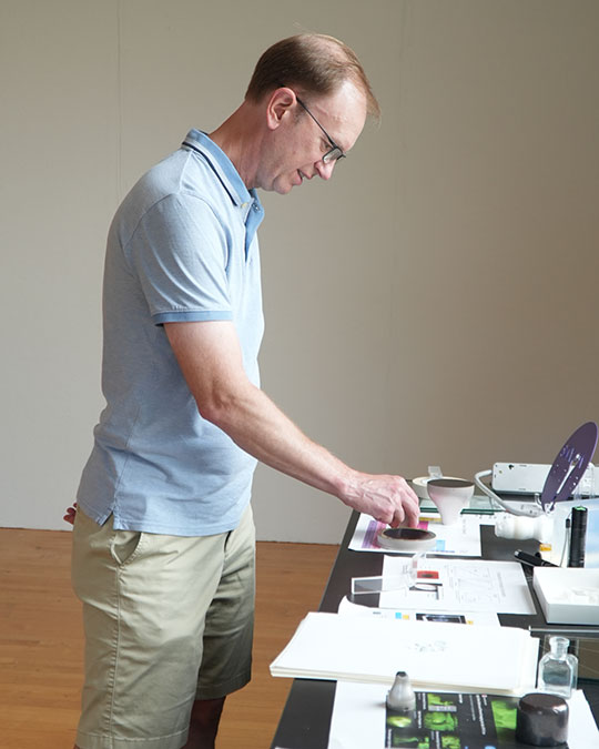 man with short sleeve shirt and glasses looking at items on a table