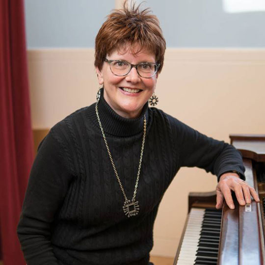 woman with glasses standing by piano