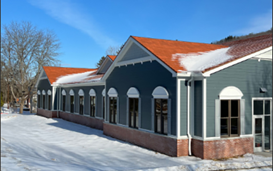 Snow-covered ground surrounds a blue-green building with red gabled roofs and white-trimmed arched windows, under a clear blue sky. Snow covers the ground around the building.
