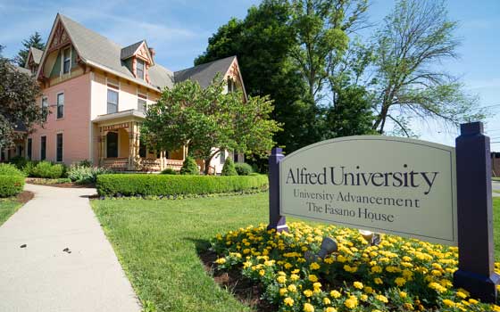 Victorian-style house with a pink exterior and large trees, framed by a sign reading "Alfred University: University Advancement, The Fasano House." Bright and welcoming.
