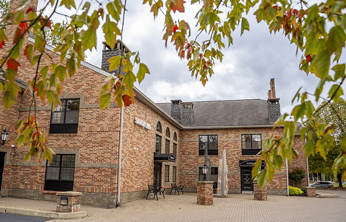 A brick building with a "Saxon Inn" sign, featuring large arched windows and chimneys. The building sits under a blue sky with scattered clouds, conveying a welcoming atmosphere.