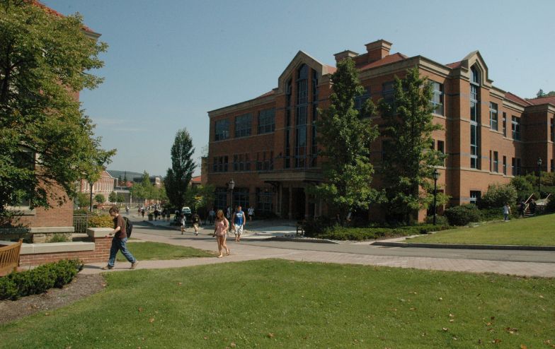 "Students walking around the Powell Campus Center at Alfred University on a sunny day, with green lawns, trees, and the brick building in the background.