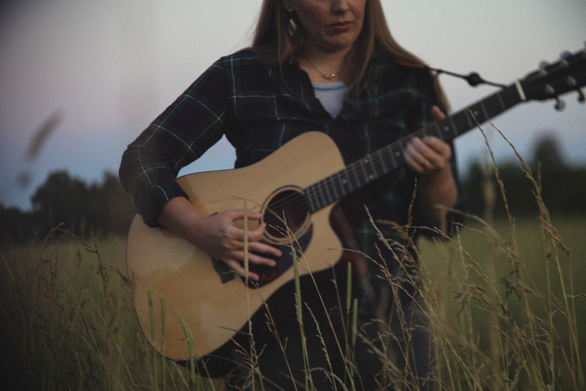 A photo of a woman playing guitar in an open field