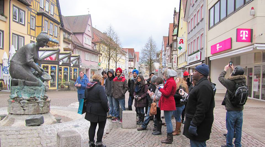 A group of Alfred University students listen to a guide at a town square during an international study tour.