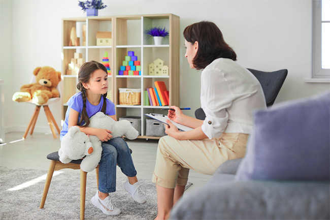 counselor talking to a small girl holding a teddy bear