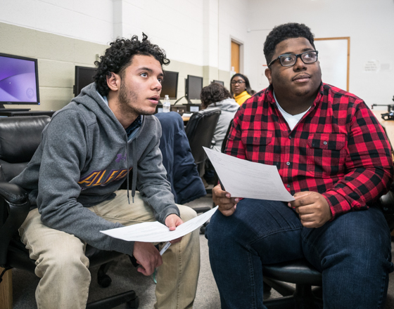 Two male students in computer lab listening to instructor