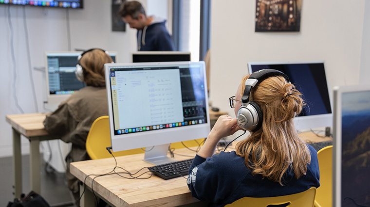 A photo of a student sitting at a computer using an audio editing software