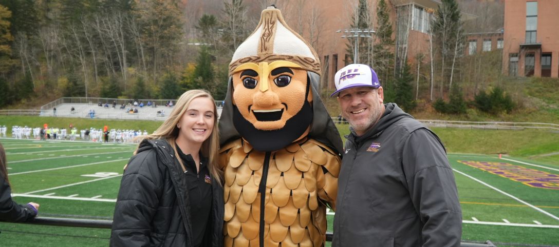 A photo of an Alfred University student and parent standing with Lil' Alf