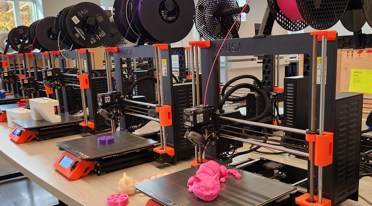 A row of 3D printers in Alfred University’s Digital Lab producing colorful printed models.