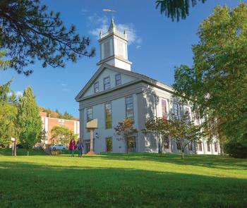 Alumni Hall at Alfred University surrounded by lush green grass and blooming trees in vibrant springtime.