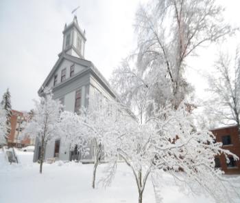 Alumni Hall stands in a snowy landscape. Surrounding trees are covered in snow, creating a serene, wintry atmosphere.