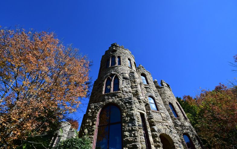 Stone exterior of the Allen Steinheim Castle at Alfred University on a snowy winter day, viewed from the base of a wooden staircase, with bare trees and snowflakes in the air.