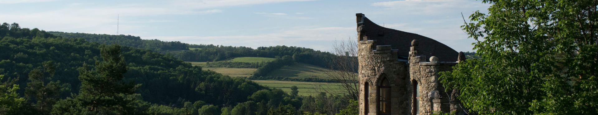 Stone castle-like building partially hidden among trees, overlooking the lush, rolling hills of Alfred, New York under a blue sky with light clouds.