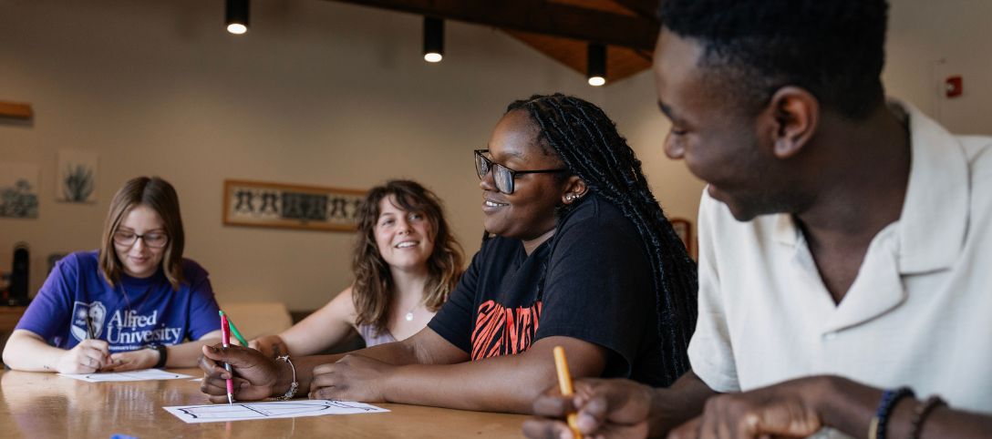 Four Alfred University students sitting around a table, smiling and collaborating on a worksheet in a bright, welcoming room at the Judson Leadership Center.