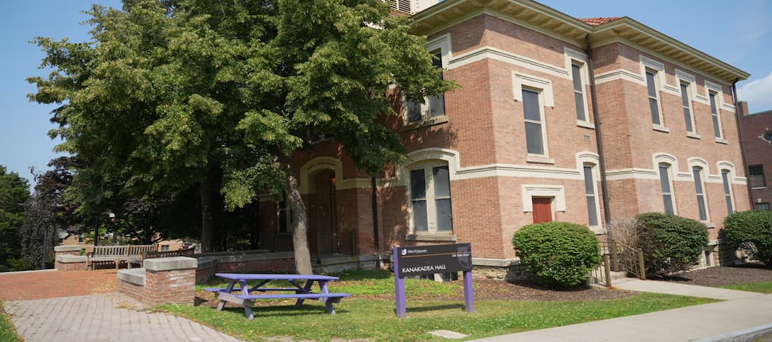 A brick building with a bench in front and a tree providing shade nearby.
