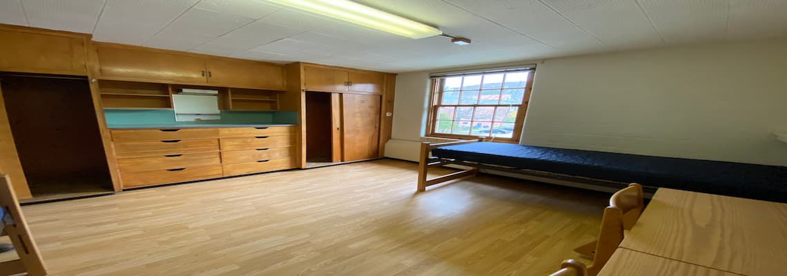A dorm room featuring a bed, desk, and cabinets, showcasing a compact living and study space for students.