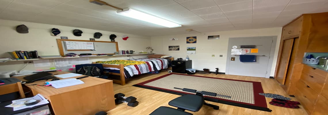 A dorm room featuring a desk, bed, and computer, showcasing a cozy and functional living space for students.