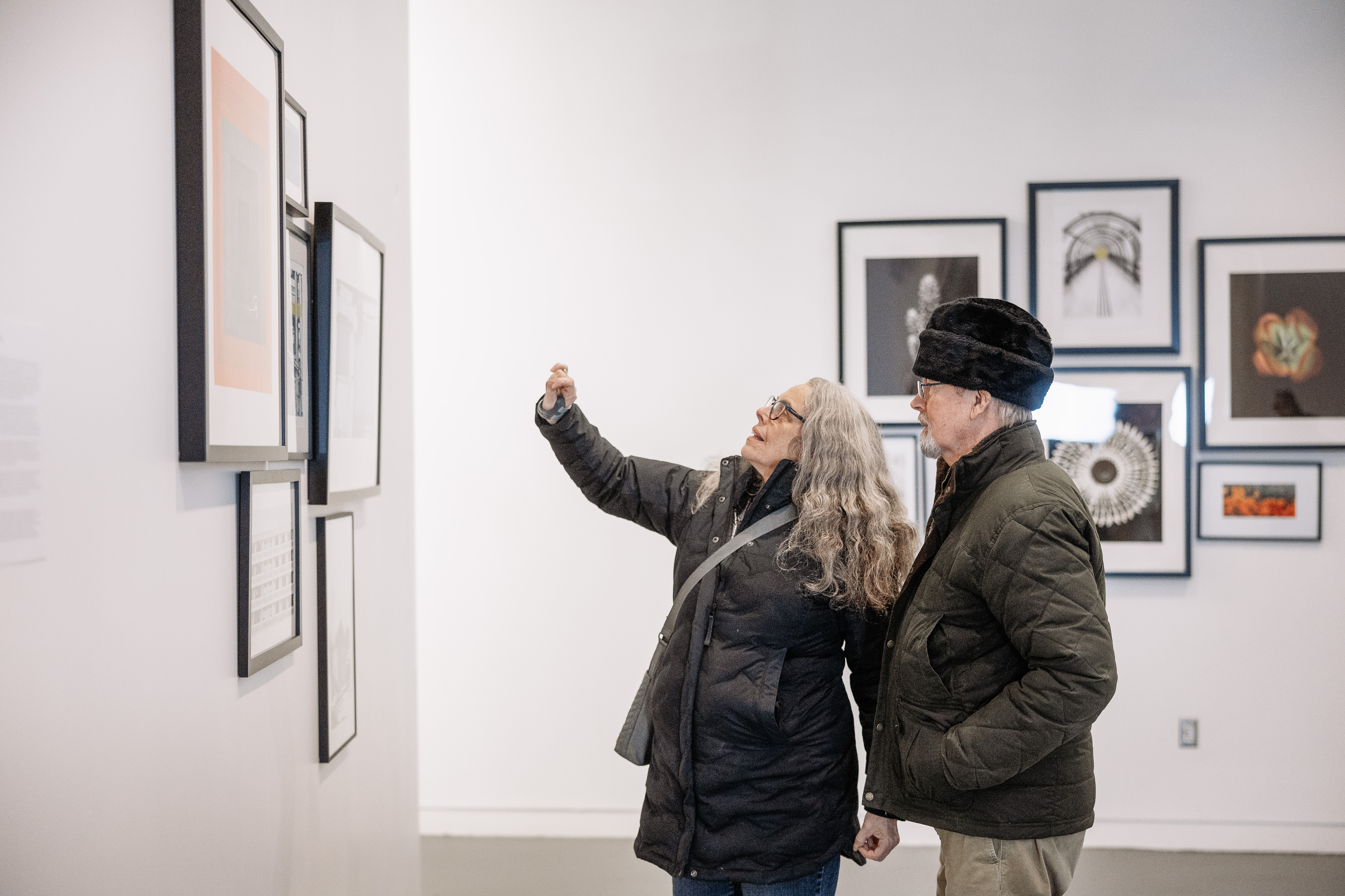 Two visitors viewing and discussing framed artwork on display in an Alfred University art gallery.