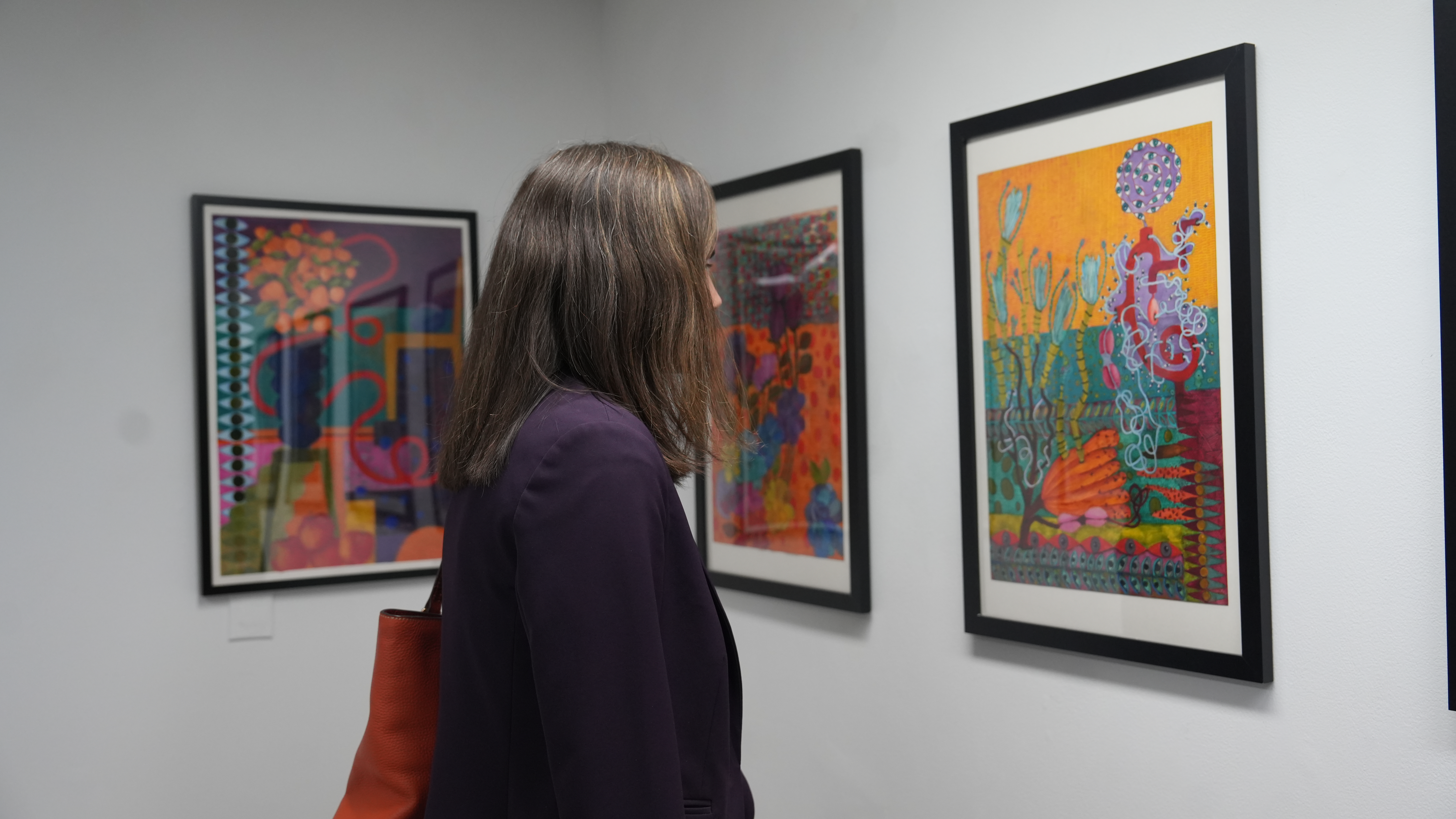 A visitor observing colorful abstract artwork framed on a gallery wall at Alfred University.