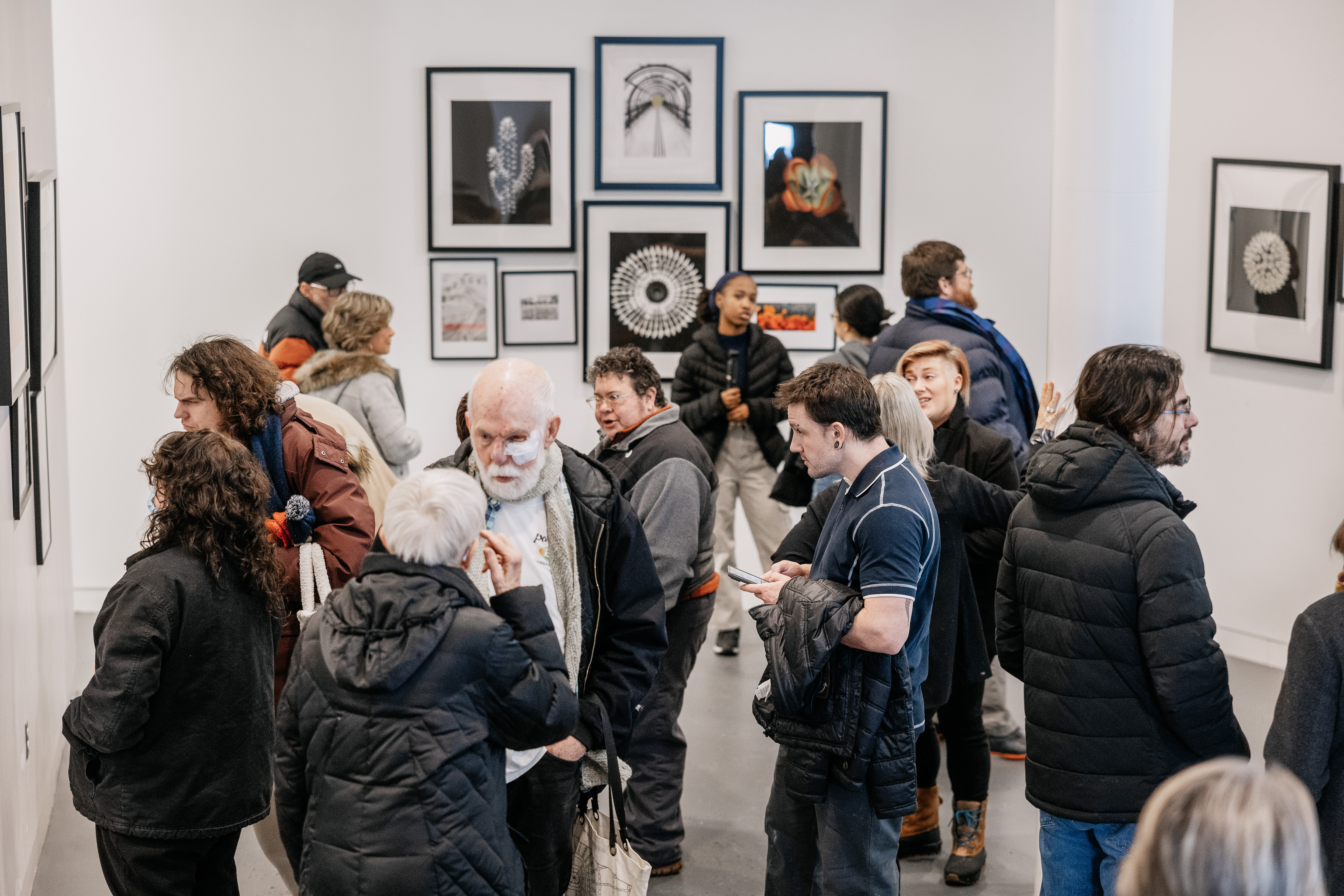 Visitors interacting and viewing artwork during an exhibition at Alfred University’s art gallery, featuring framed photographs and prints on white walls.