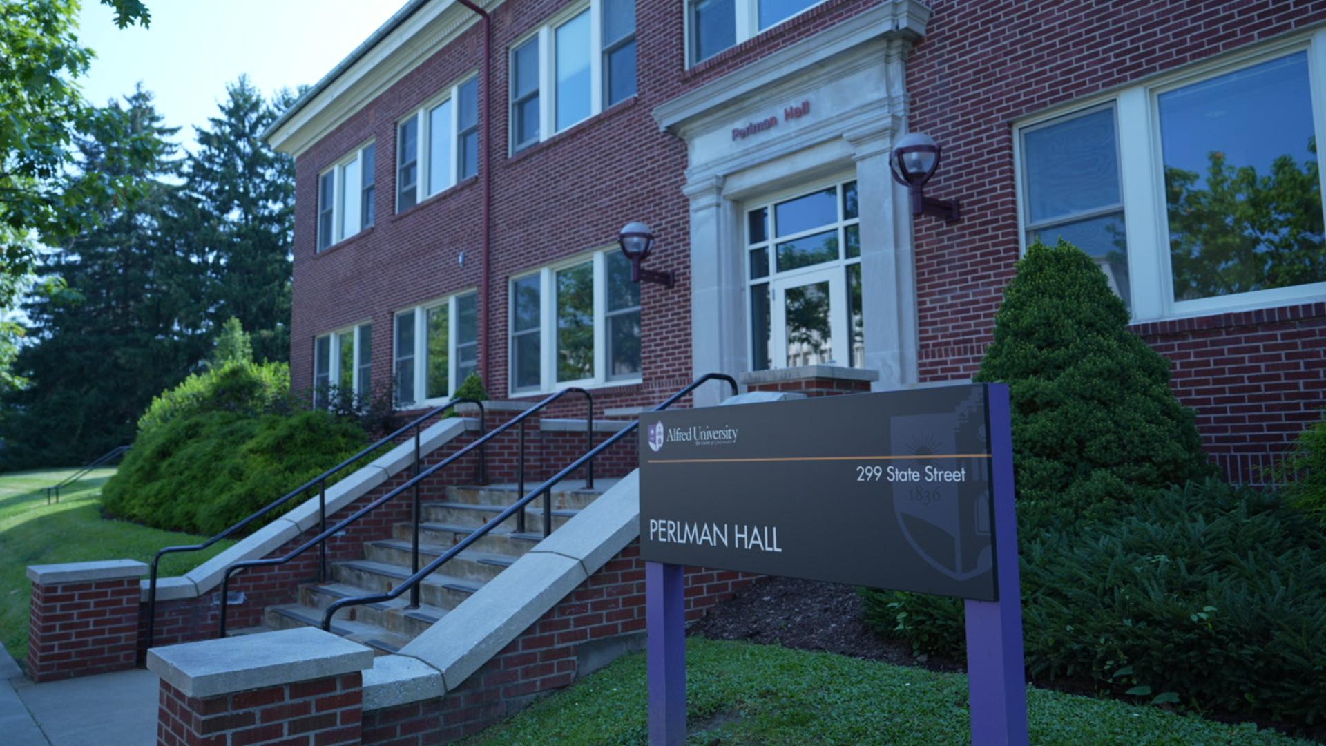 A brick academic building with large windows and a sign in front reading "Perlman Hall, 299 State Street." Steps lead to the building entrance.