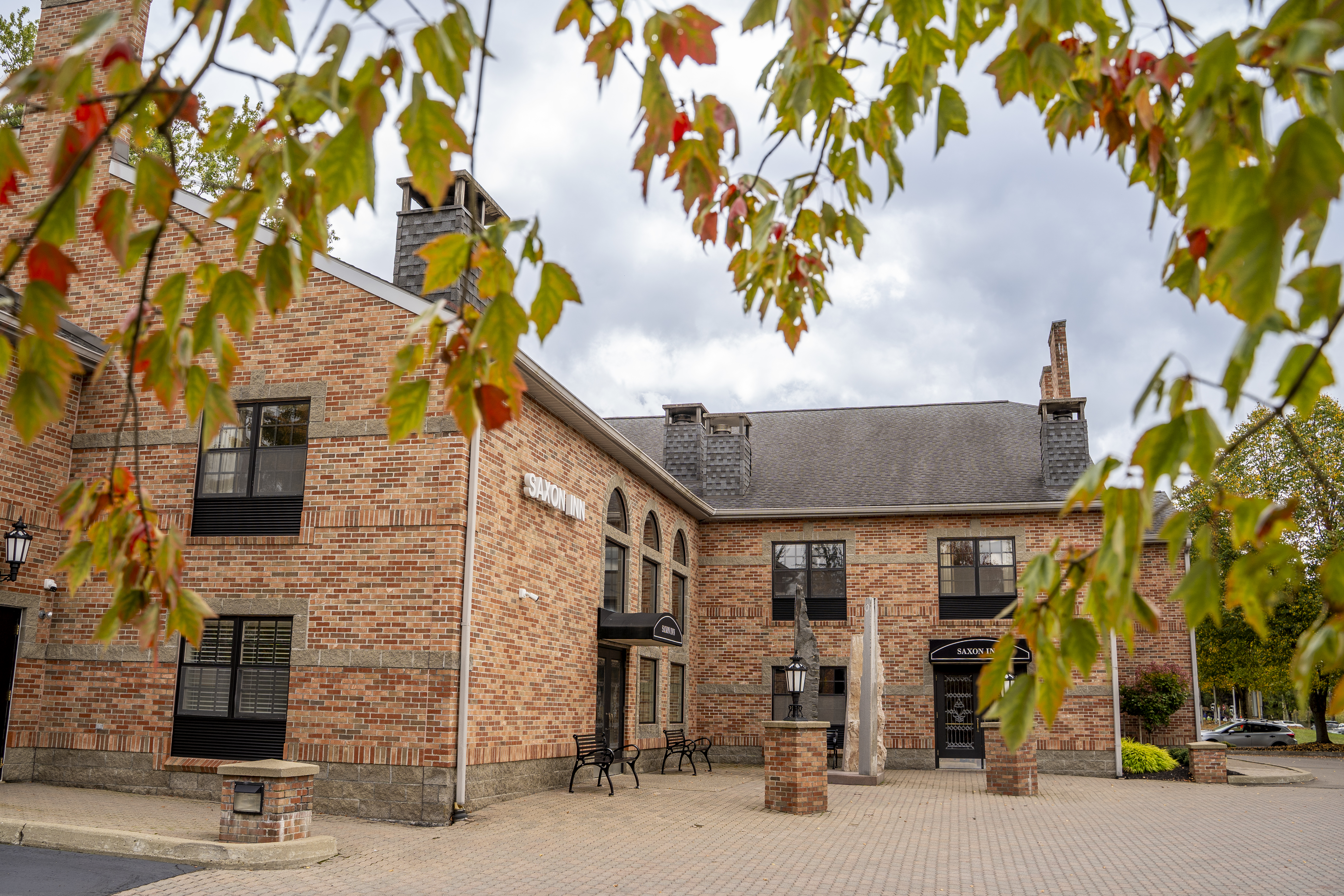 A brick building with a "Saxon Inn" sign, featuring large arched windows and chimneys. The building sits under a blue sky with scattered clouds, conveying a welcoming atmosphere.