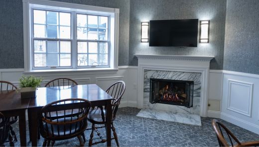 Elegant sitting area at the Saxon Inn with a wooden dining table, a marble fireplace, a mounted TV, and large windows letting in natural light.