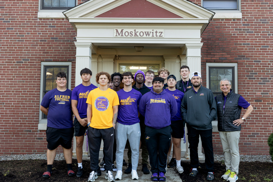 Group of Alfred University football players and staff posing in front of Moskowitz Hall during Welcome Week