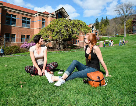 A photo of two Alfred University students sitting on the grass in front of Powell Campus Center