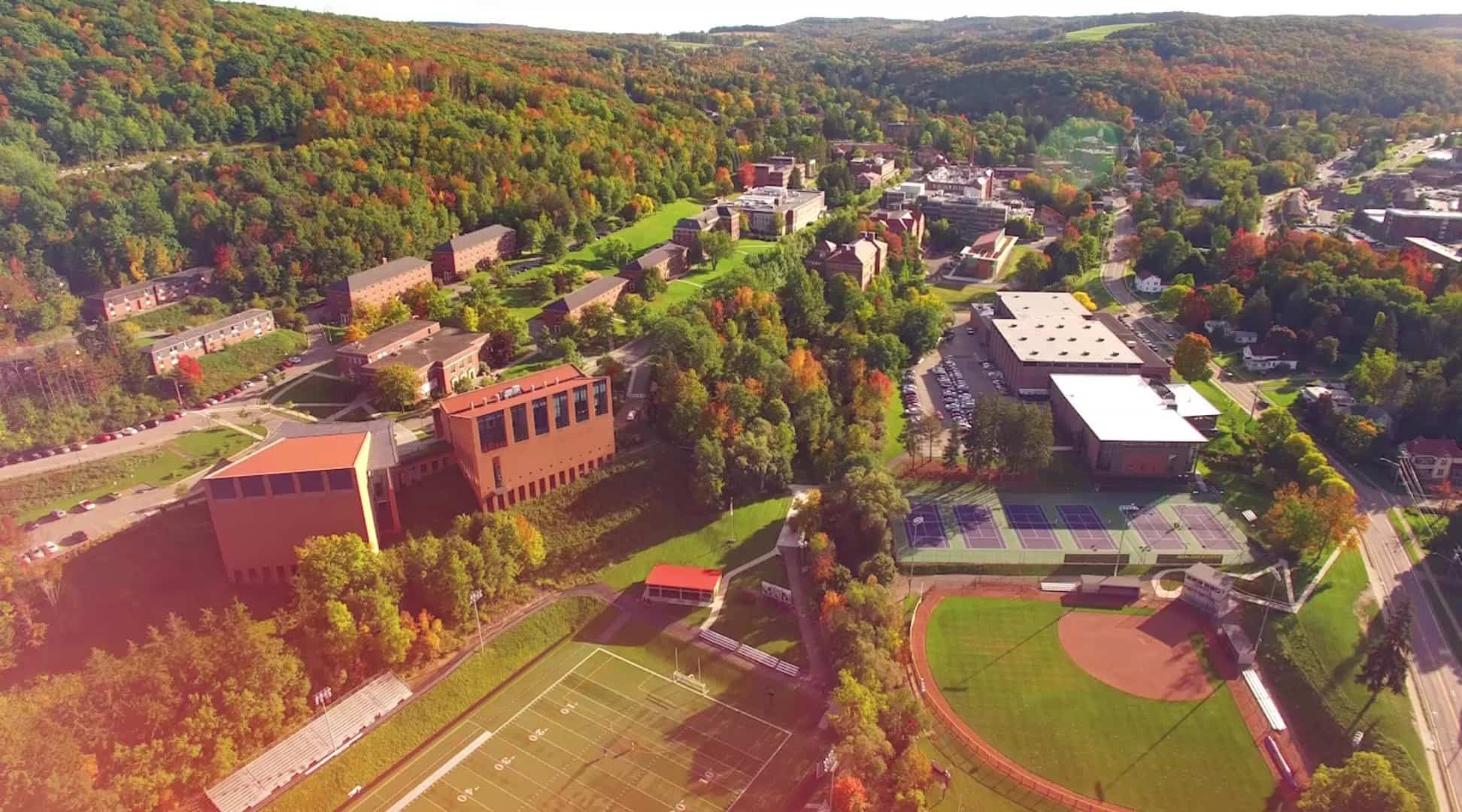 Aerial view of a small town nestled in lush green hills under a vibrant sunset sky with pink and purple clouds, conveying a serene, picturesque landscape.