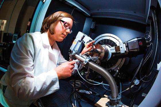  A researcher in a white lab coat operates advanced scientific equipment in a ceramics lab at Alfred University, adjusting a component of a high-tech analysis machine.