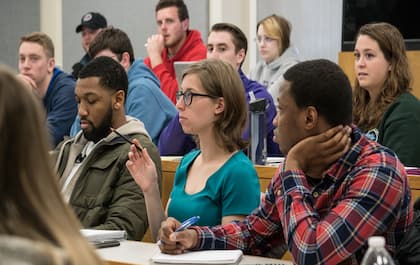 A group of students in a classroom setting with one raising their hand preparing to answer a question.
