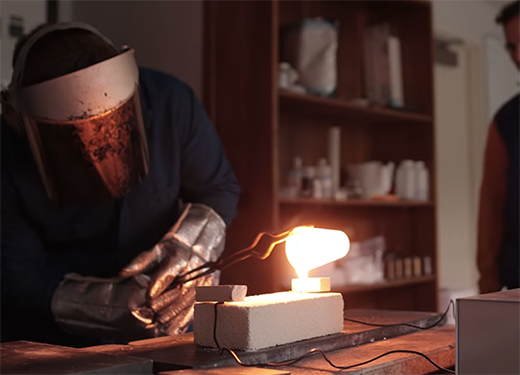A photo of an Alfred University student working with molten glass