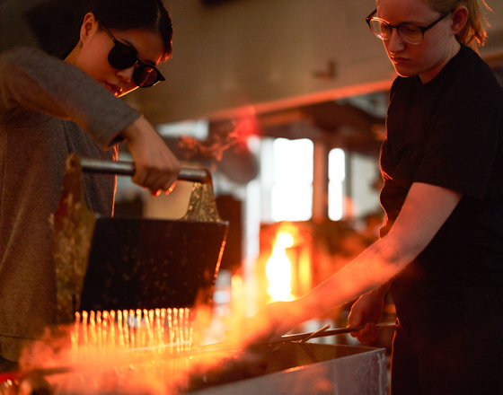 two students working with hot glass in the studio