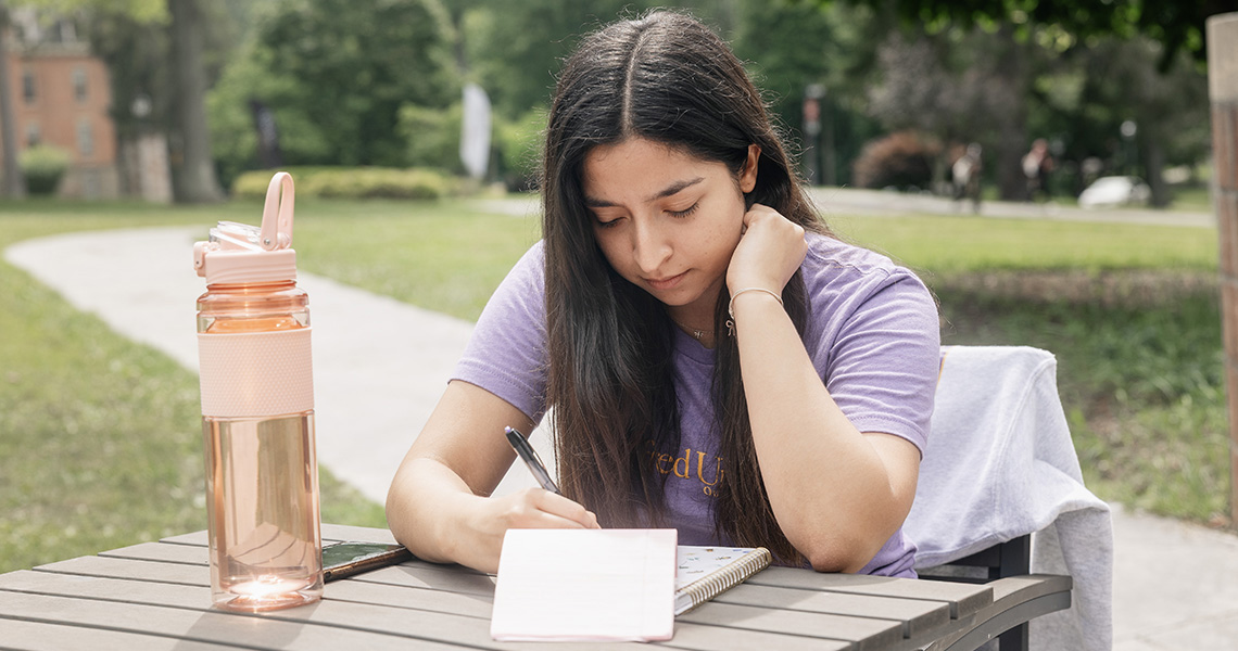 A photo of an Alfred University student writing in a notebook
