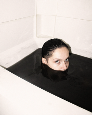 art photograph person in bathtub filled with black liquid, only eyes and nose visible above the liquid
