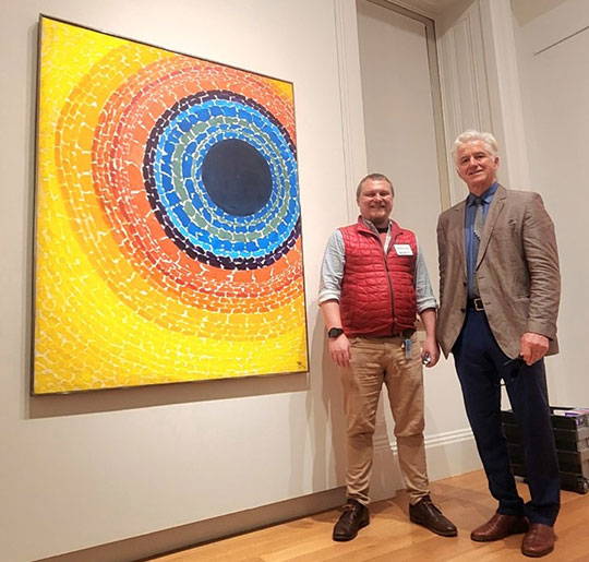 two men standing by a piece of artwork