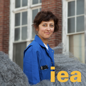 headshot of brown haired person in blue coverall with iea logo over laid