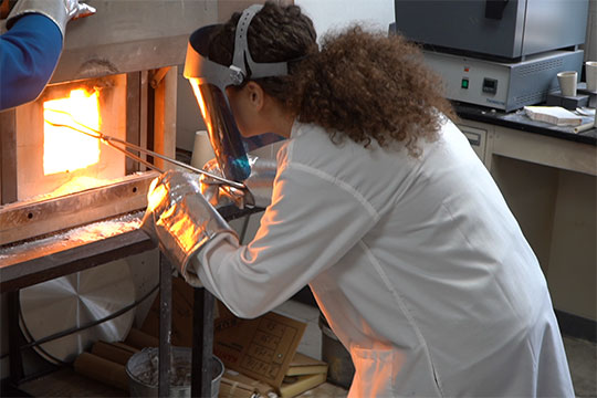 woman in lab coat removing material from furnace