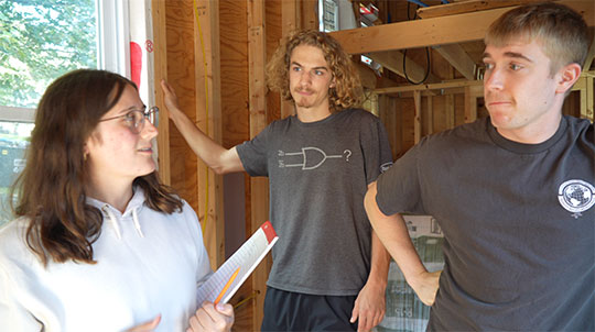 three students (woman, man, man, left to right) in tiny house