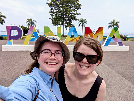 two women, smiling, in front of Panama sign