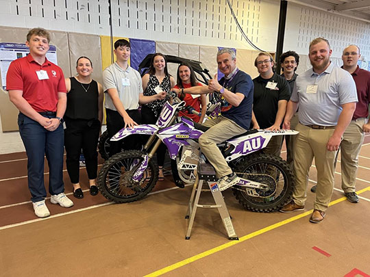 group of people standing around a motorcycle with man sitting on motorcycle