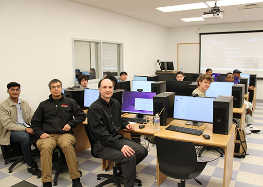 large group of people at computer stations, looking at the camera