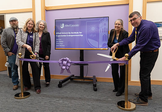 four people standing in a row, smiling, cutting a ribbon