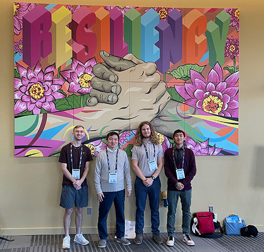 four people standing in front of a mural