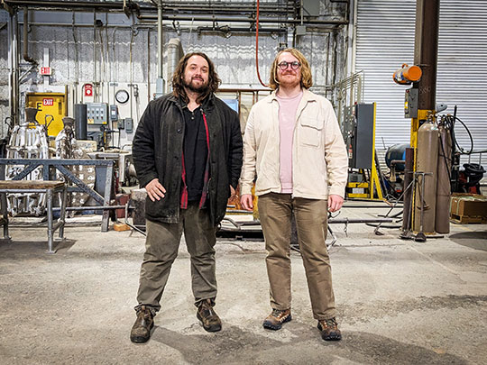 two men with beards standing in a foundry facility