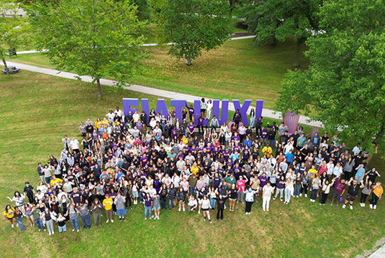 large group of people gathered on a lawn near a sign