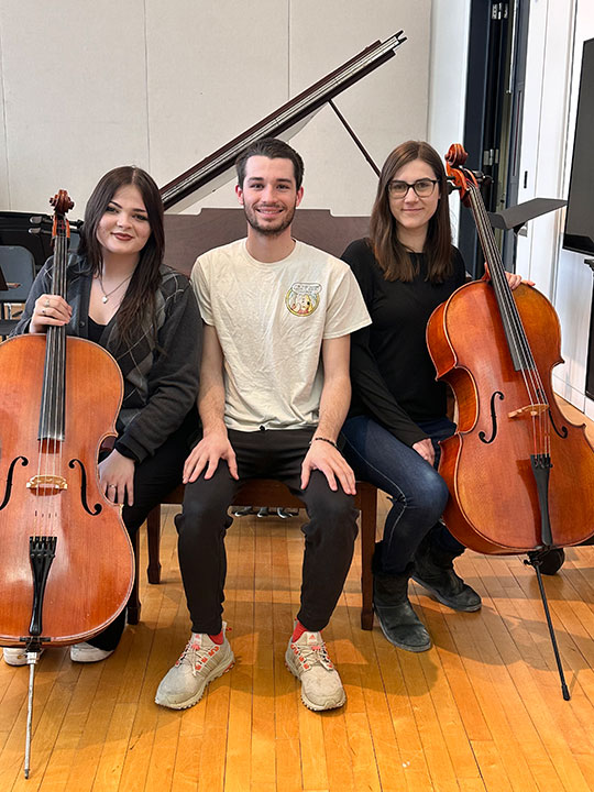 three people sitting, two holding cellos